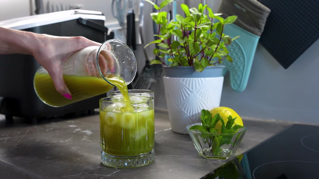 Ev yapımı naneli limonata, bir bardağa buz üzerine dökülürken, mutfak tezgahında taze limon ve nane ile ferahlatıcı bir yaz içeceği teması için yakın çekim görünüm.