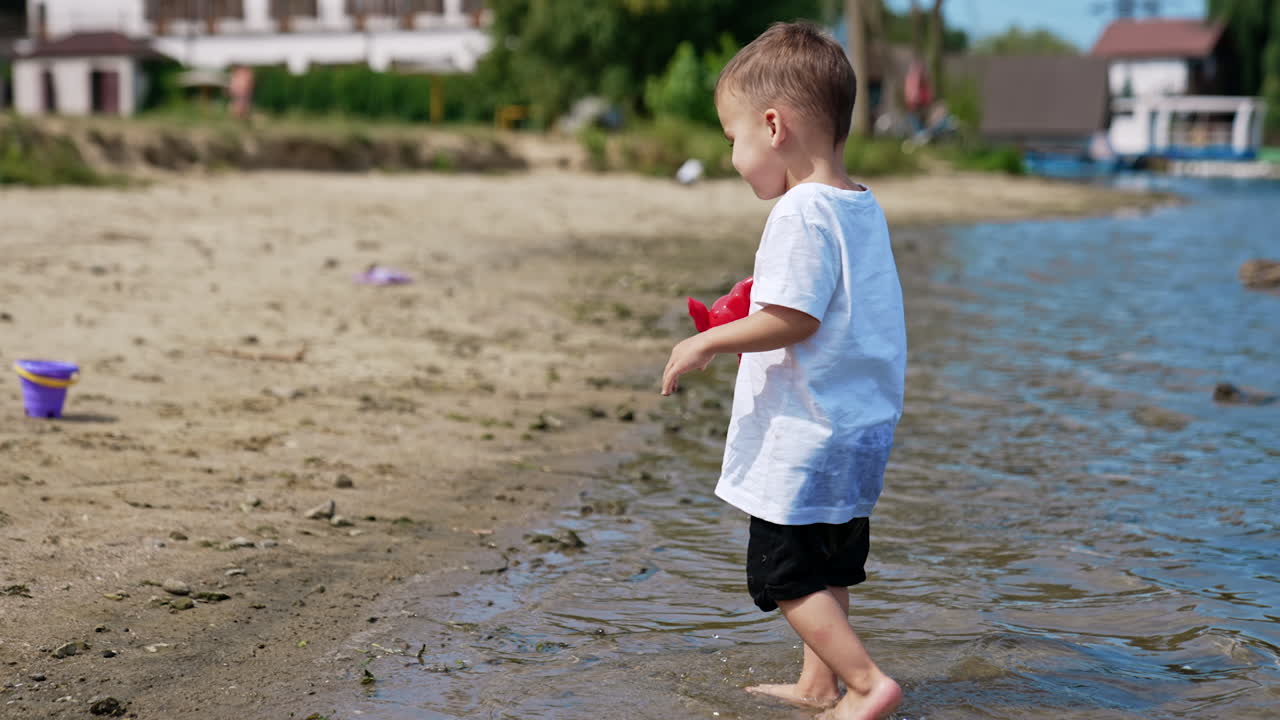 Beautiful smiling kid carries water from the sea in his watering can. Adorable toddler boy goes to his bucket on the sandy beach.