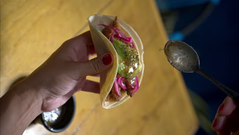 vertical slow motion of a woman holding a shrimp seafood taco with red onion and avocado serving pouring green salsa sauce on top at a traditional mexican restaurant