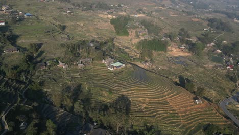 Aerial-drone-shot-of-villages-amidst-bright-green-rice-terraces-in-the-mountains-of-Sapa,-Vietnam