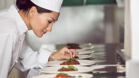 Una-Chef-Asiática-Sonriente-Con-Delantal-Preparando-Comida-En-Una-Cocina-Profesional.