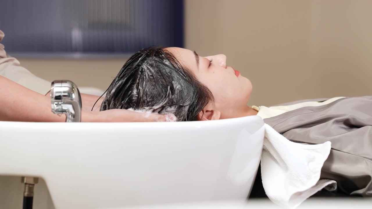 Un parrucchiere lava i capelli di una cliente, prima di applicare ingredienti naturali ristrutturanti e vitamine per il taglio. La cliente si gode il lavaggio dei capelli in salone con un massaggio rilassante con shampoo