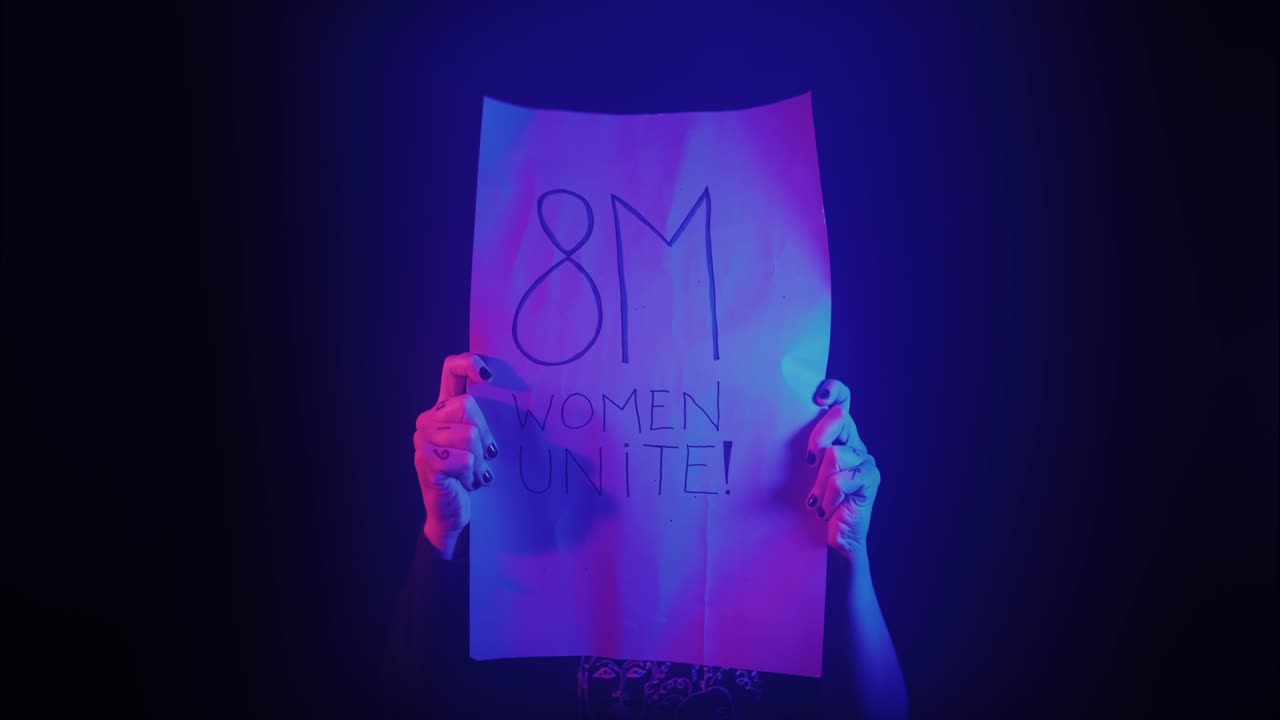 Woman Holding '8M Women Unite!' Protest Sign in Neon Light