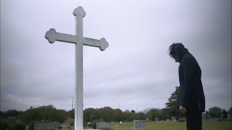 young, religious man in black suit worshipping and praying in front of christian cross