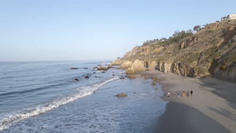 people walking on el matador beach at sunrise, malibu in california