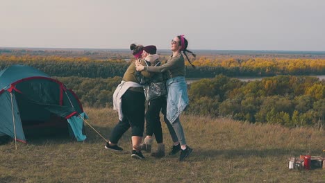 happy girls hug and spin near tent and campfire in autumn