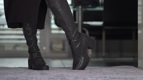una mujer vestida con botas negras brillantes está haciendo una presentación en su alfombra