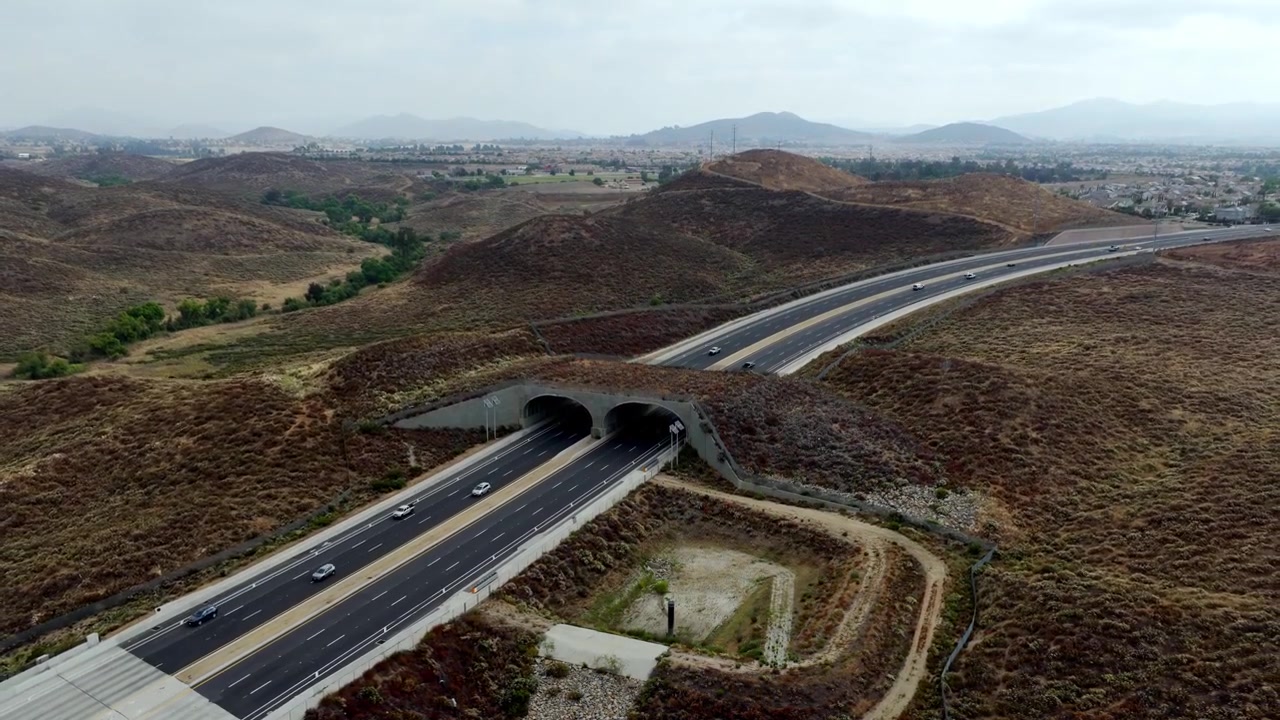 Le auto viaggiano attraverso un tunnel nella Temescal Valley, California, circondate da dolci colline e montagne distanti. Utile per progetti infrastrutturali o studi sui trasporti.