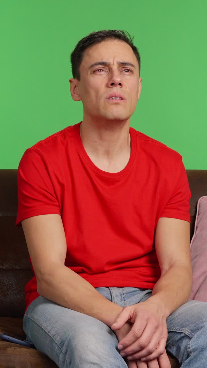 Sad man sitting on sofa, waiting for message on green screen