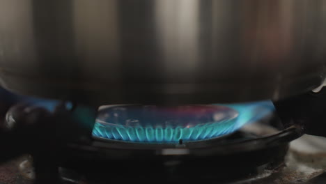 close up of stainless steel pot placed securely on gas burner as cooking begins with flame ignited underneath, focusing on bottom of pot and burner details in a home kitchen environment
