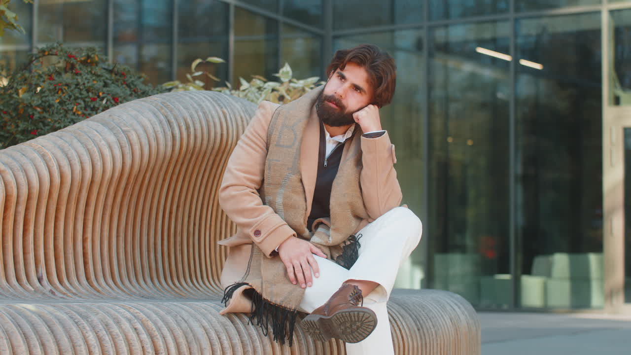 Sad unhappy frustrated indian man sitting alone in city street feeling bad annoyed grief problem