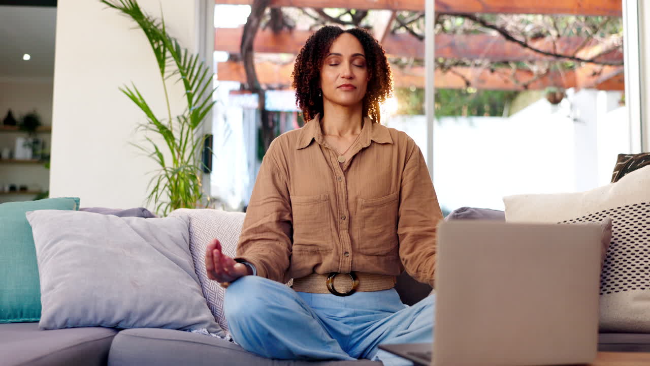 Woman meditating on couch with laptop