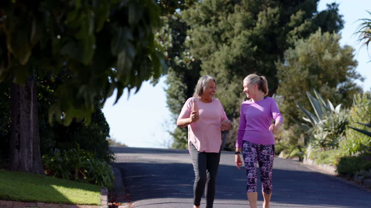 Multiracial female friends walking and talking outdoors, enjoying sunny day together, copy space