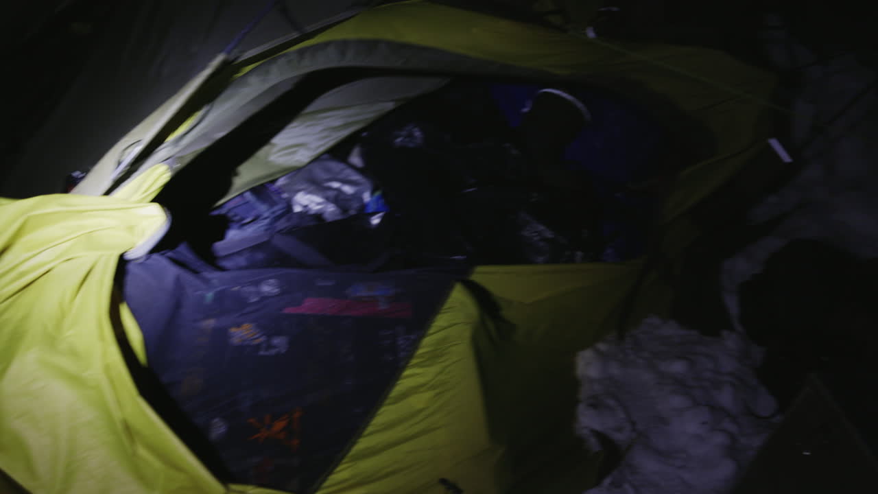 Interior tent illuminated by headlamp during winter night camping, rough winds blow and spread gear everywhere in panic