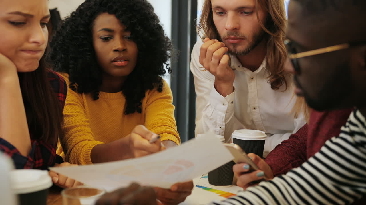 Close-up view of multiethnic coworkers viewing graphics and taking notes sitting at a table in a cafe