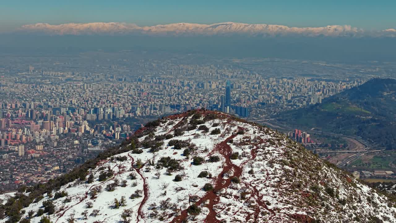 Panoramic view of snowy hilltop with Santiago city below and Andes mountains in the distance
