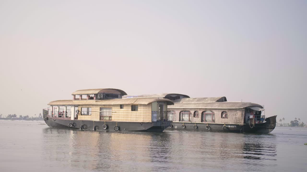 카메라는 늦은 오후의 태양 아래 케랄라 백워터처럼 유리를 따라 활공하는 앞쪽에 있는 두 척의 하우스보트와 비슷한 속도로 항해합니다.