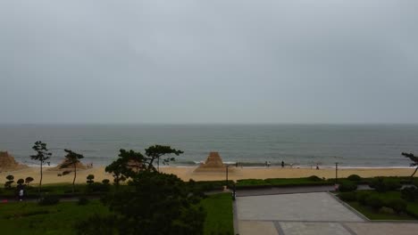 aerial de la escultura de playa de arena en nanhai china, avión no tripulado que asciende revelando playa de arena con olas del océano en el smog aire contaminado ciudad de china