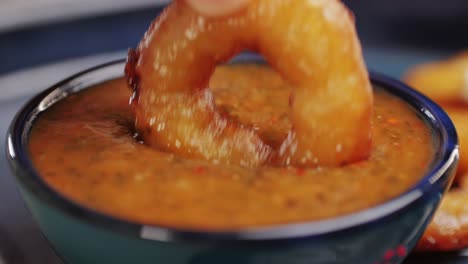 fried crispy onion rings dipping in red salsa ketchup sauce close-up macro. roasted onion rings for snacks at bar, cafe. fast food. delivery. beer snacks