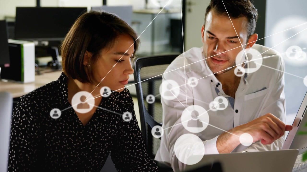 Man gesturing at laptop, woman noting, network visualization expanding over business collaboration