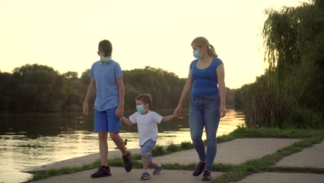 a family with a child in medical masks walk near the lake 01