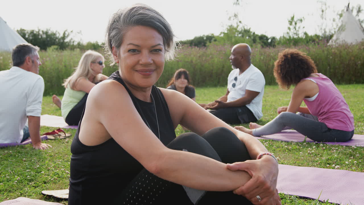 Ritratto di donna matura durante un ritiro yoga all'aperto con amici e campeggio sullo sfondo
