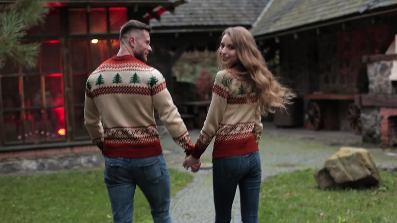 Smiling couple coming closer to the country house. Pair in similar clothes walking near the beautiful village manor.