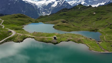 dramatic-tilt-aerial-view-of-blue-mountain-lake-in-the-swiss-alps-with-dramatic-snow-covered-mountain-peaks-backdrop,-Bachalpsee-Grindelwald-First,-Switzerland