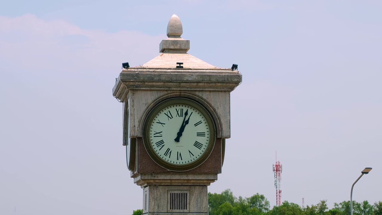 A classic clock tower stands tall against a clear sky, with lush greenery in the background. Suitable for historical documentaries or urban landscape projects.