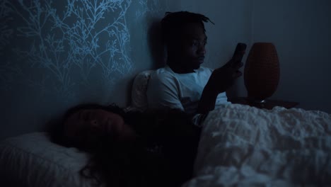hombre se sienta en la cama tarde en la noche desplazándose a través de las redes sociales en un teléfono inteligente