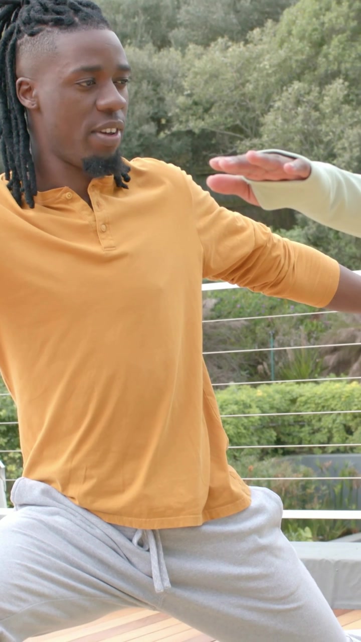 Video verticale: Una mano guida un uomo che si mette in affondo su un tappetino verde sul ponte, con un top color senape per bilanciarsi
