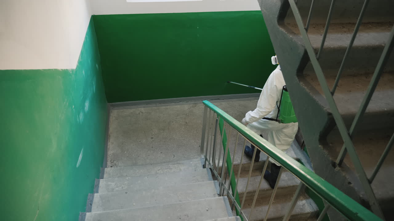 trabajador con ropa protectora rocía las escaleras de un edificio de apartamentos con antiséptico 1