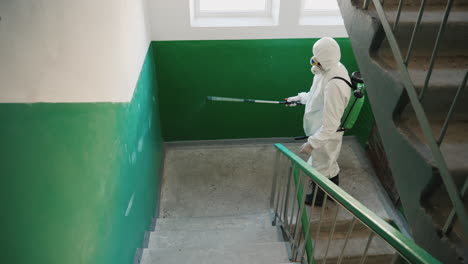 trabajador con ropa protectora rocía las escaleras de un edificio de apartamentos con antiséptico 1