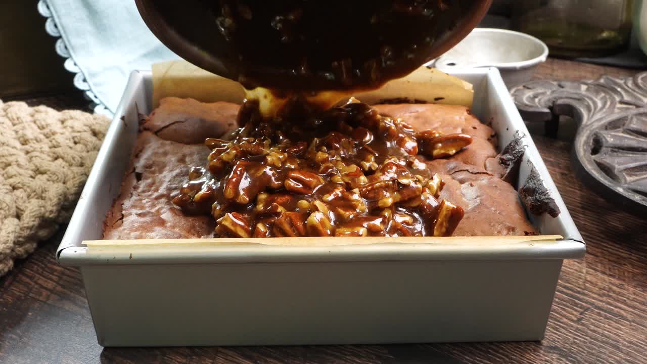 Baking delicious caramel pecan brownies. Pouring the caramel pecan topping over the brownie in a square baking pan. Freshly baked gooey chocolate brownies with sweet caramel and nutty pecans.