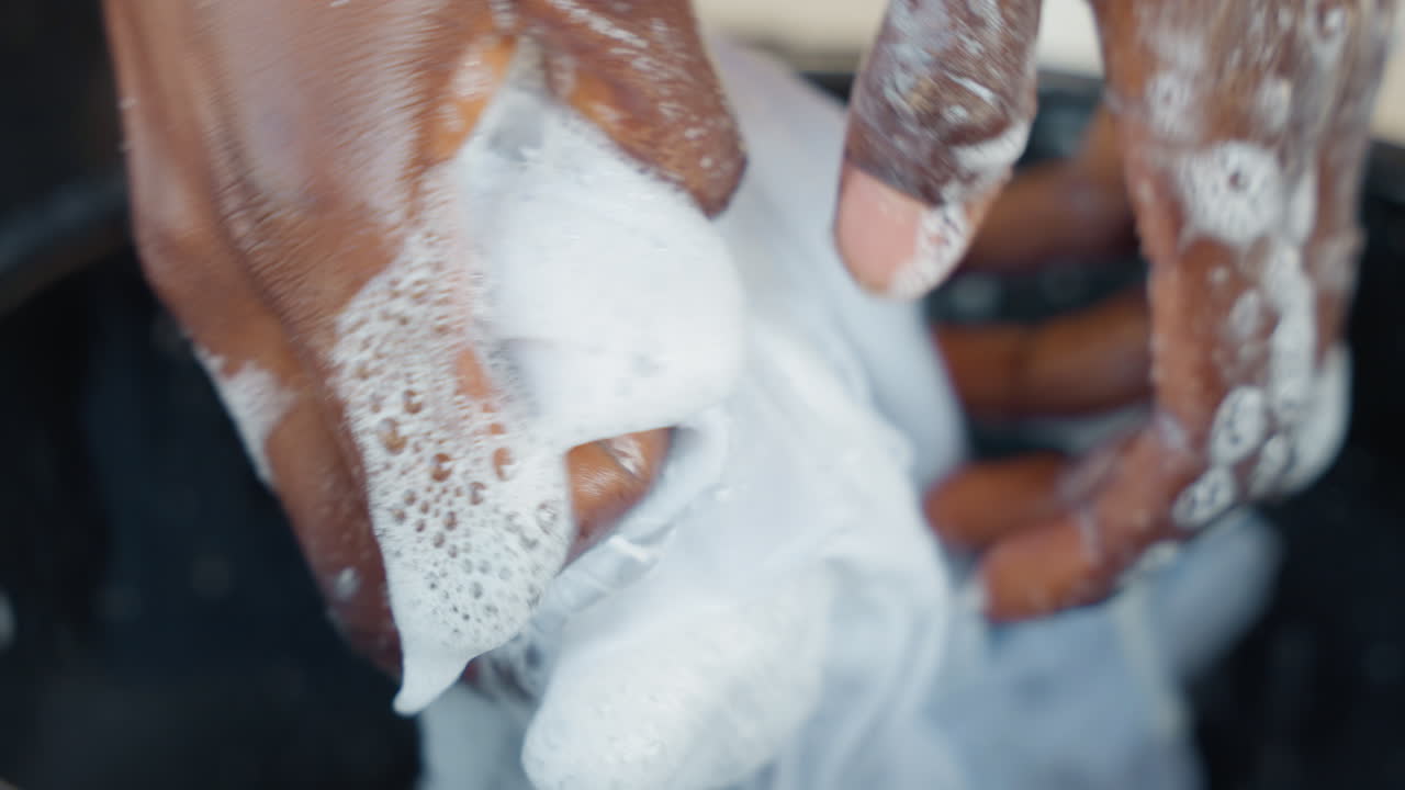 Attività in cortile urbano di pulizia di tessuti con acqua. Persona che sciacqua materiale bianco con sapone in uno spazio esterno illuminato dal sole. Operaio nel cortile cittadino lava e strizza accuratamente il tessuto con acqua e sapone.