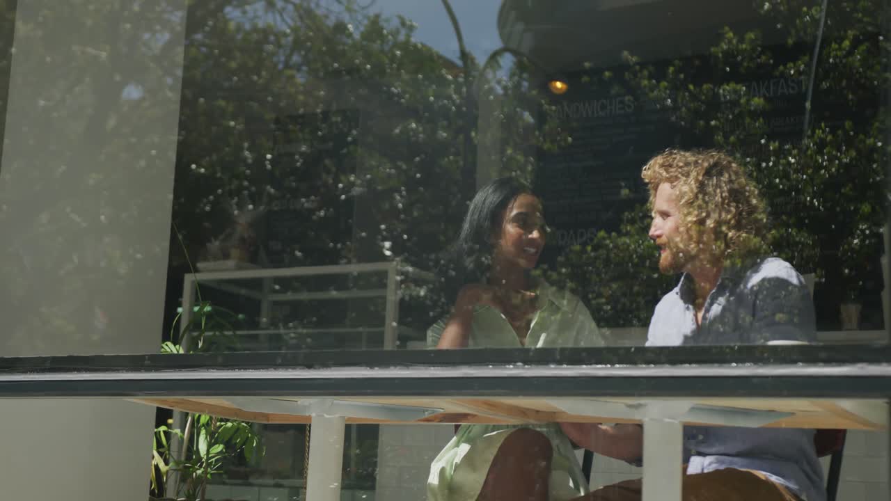 pareja feliz y diversa sentada a la mesa y hablando en una cafetería