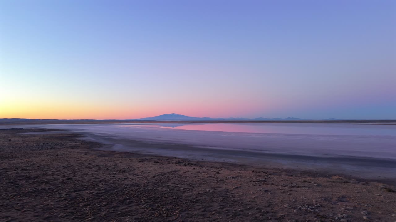 Drone fly at tranquil Salinas del Diamante salt lake with mountain silhouette in distance under colorful sky, Mendoza, Argentina