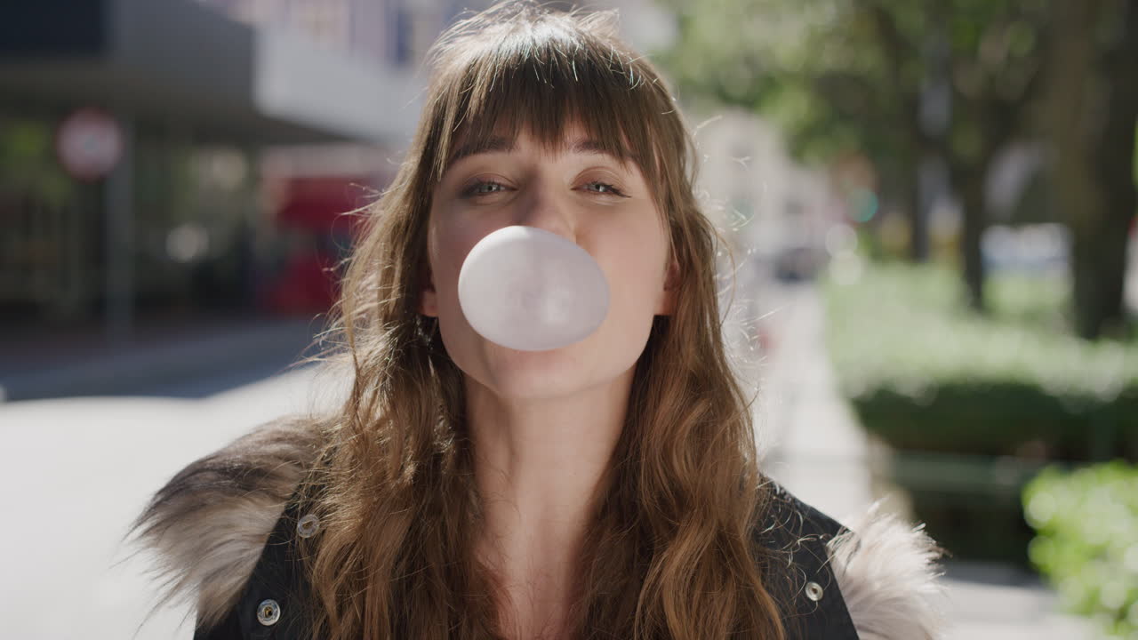 retrato de una hermosa mujer joven soplando chicle sonriendo feliz disfrutando de diversión lúdica en una vibrante calle de la ciudad urbana por la mañana