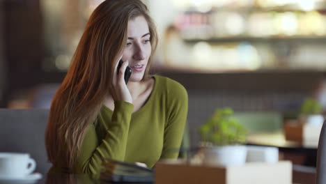 Attractive-young-woman-is-sitting-in-a-cafe-indoors-and-talking-on-the-phone