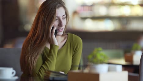 una joven atractiva está sentada en un café adentro y hablando por teléfono