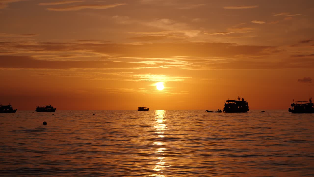 Fishing boats rest on calm waters as the golden sun sets over Ko Tao, reflecting across the horizon
