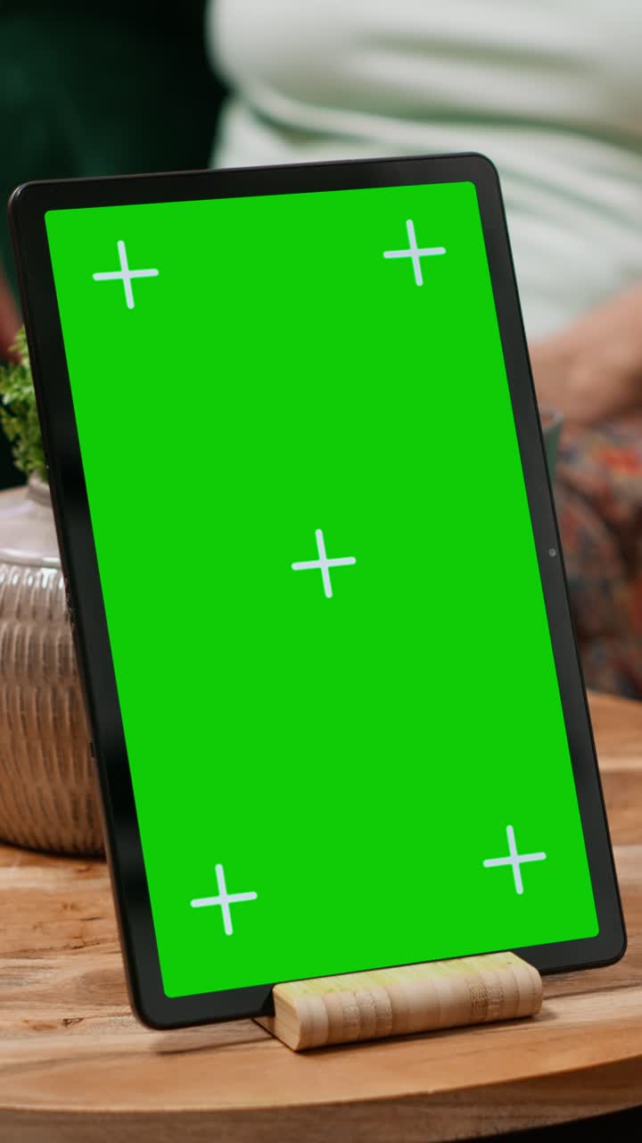 Verticale video: Oudere man en vrouw praten thuis met een groen scherm op een tablet
