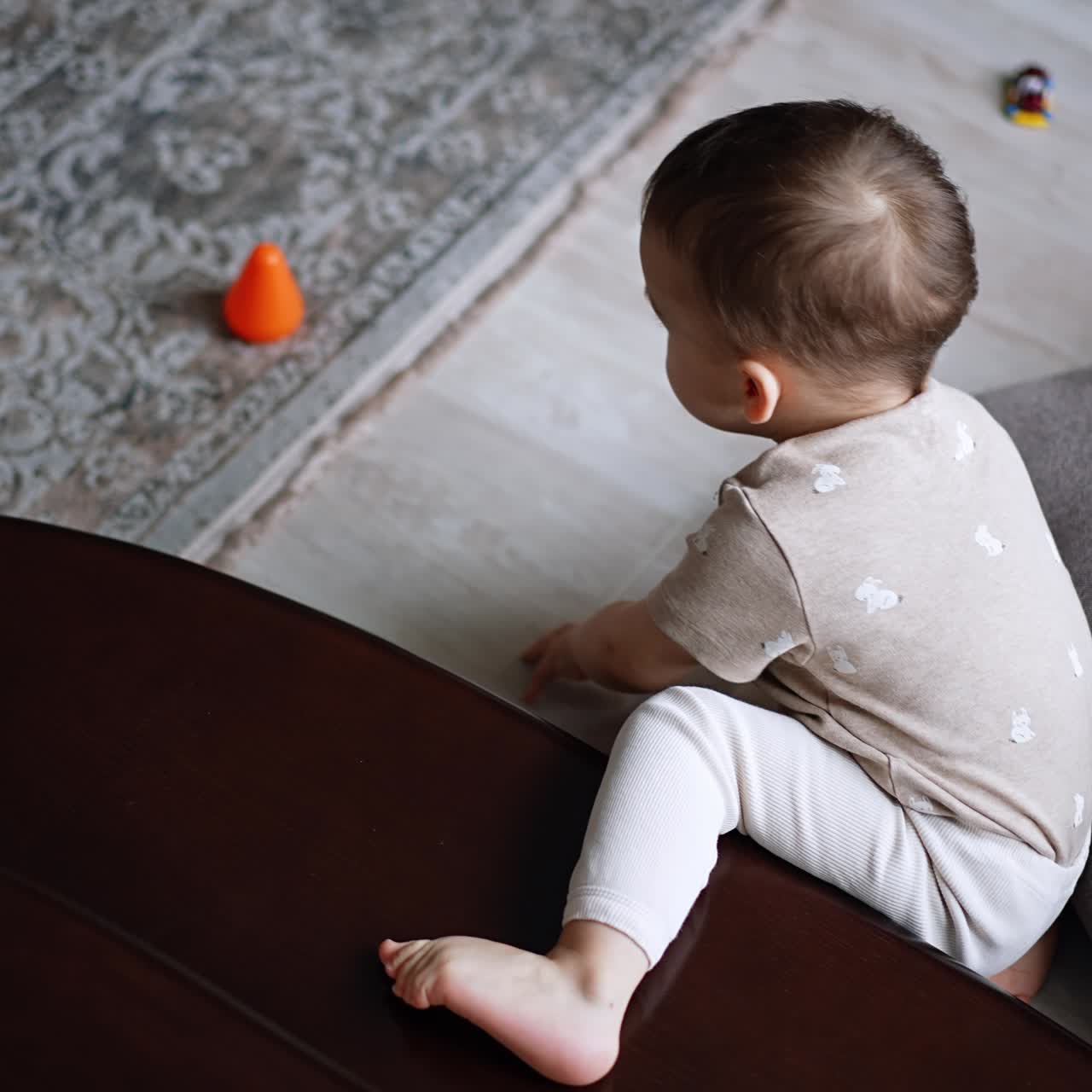 Toddler boy crawls by the stairs in the room. Kid gets off the step and sits down on the floor near the cushion. Top view