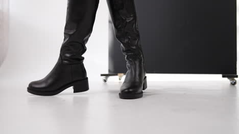 elegant black eco leather boots on middle size heels. model demonstrates stylish footwear at white backdrop. close up.