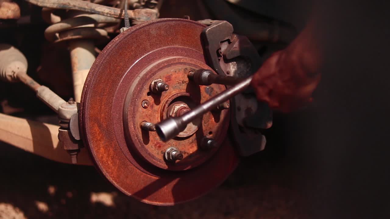 Close-up of mechanic loosening rusty wheel hub nuts on disc brake using wrench.