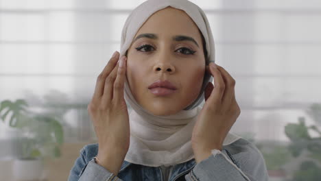 close up portrait of young muslim business woman looking at camera busy preparing headscarf in office workspace background