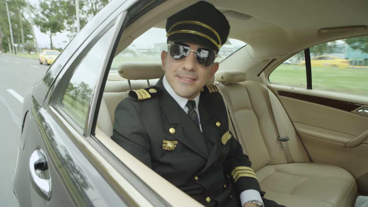 A pilot use glasses sits in a seat inside a black car that drives him