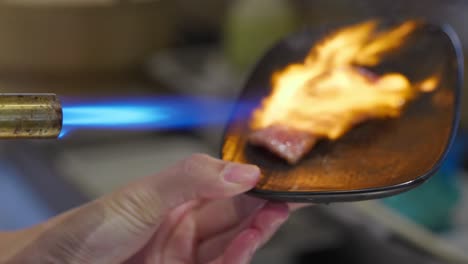 a seared beef aburi sushi being blow torched with a flame on a black plate in a japanese restaurant