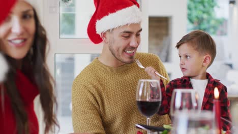 Hijo-Caucásico-Dándole-Comida-A-Su-Padre-Con-Un-Tenedor-Durante-La-Comida-Navideña