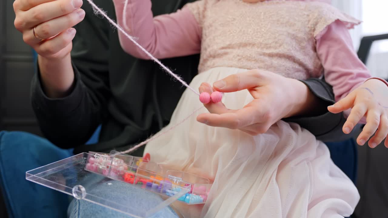 Father and daughter making necklace from beads, close up
